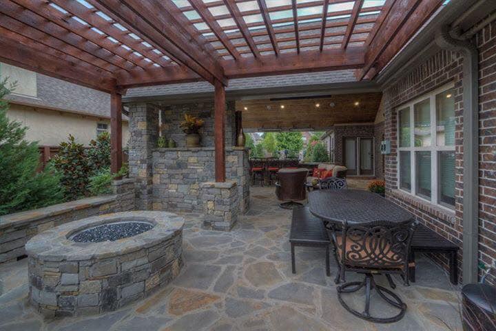 A patio with a fire pit , table and chairs under a pergola.