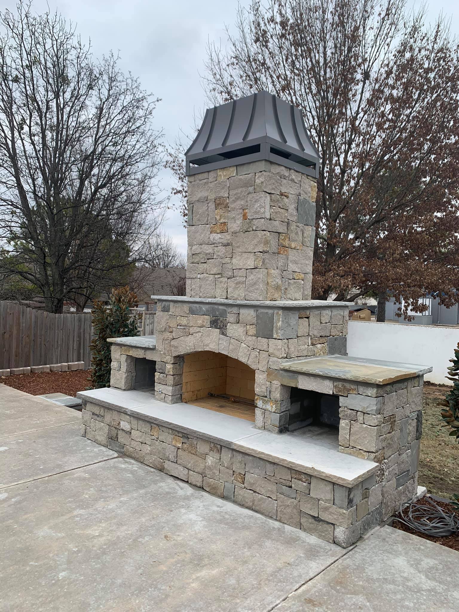 A large stone fireplace is sitting on top of a concrete patio.