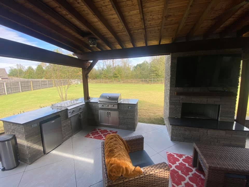 A covered patio with a grill , fireplace and television.