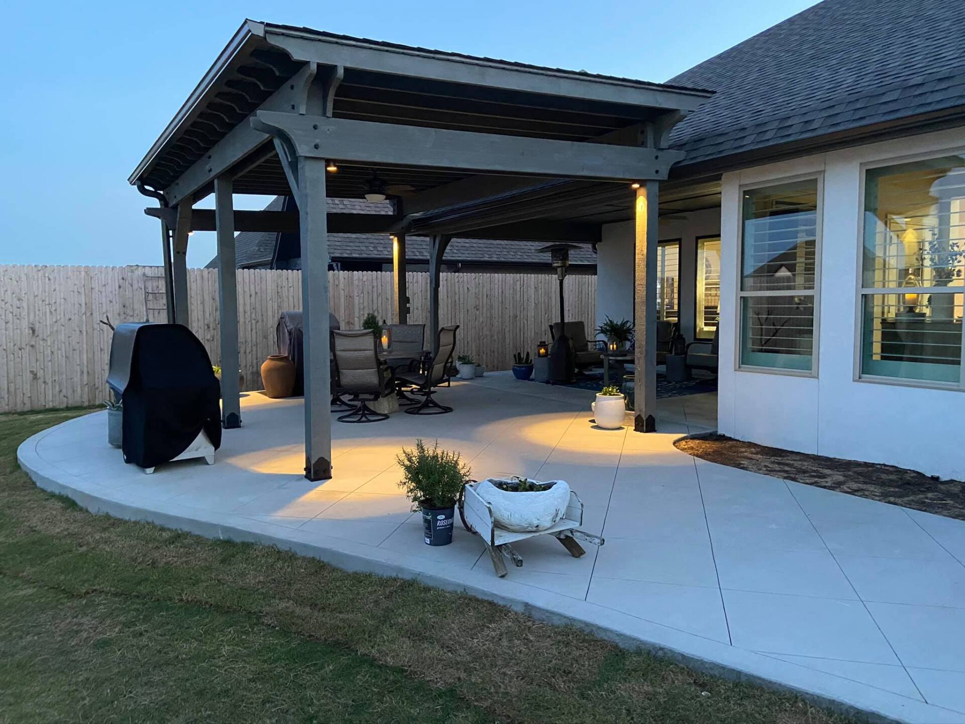 A patio with a pergola and a grill in front of a house.