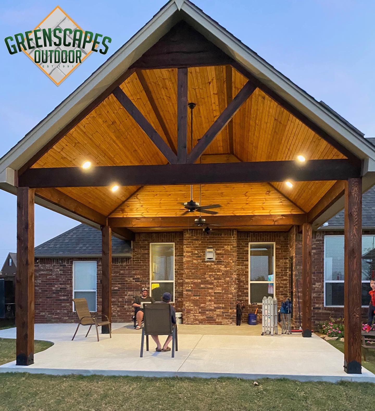 A brick house with a covered patio and a greenscapes outdoor logo
