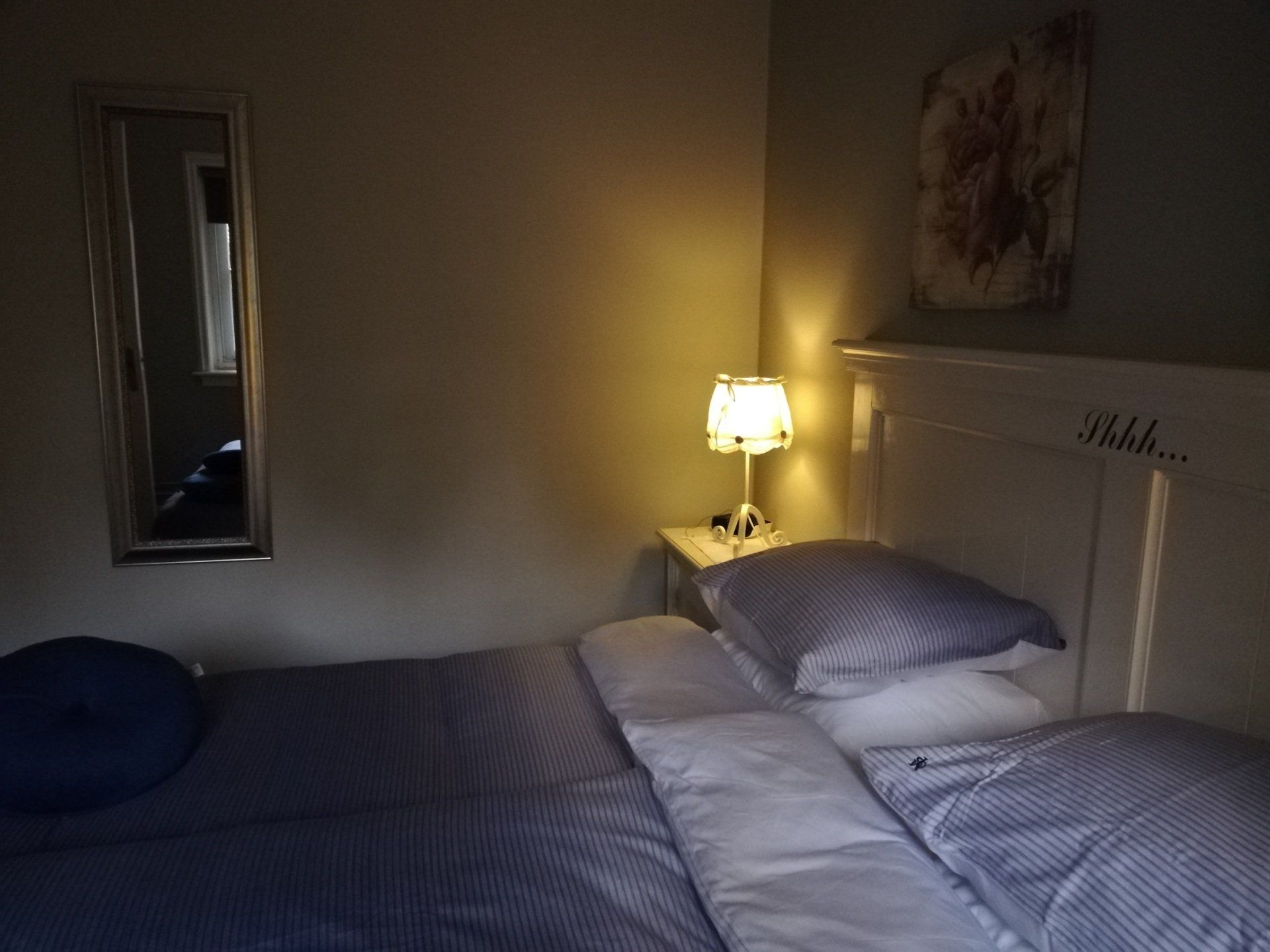 Slaapkamer met bed, lamp op het nachtkastje, spiegel aan de muur, schilderij boven het hoofdeinde.