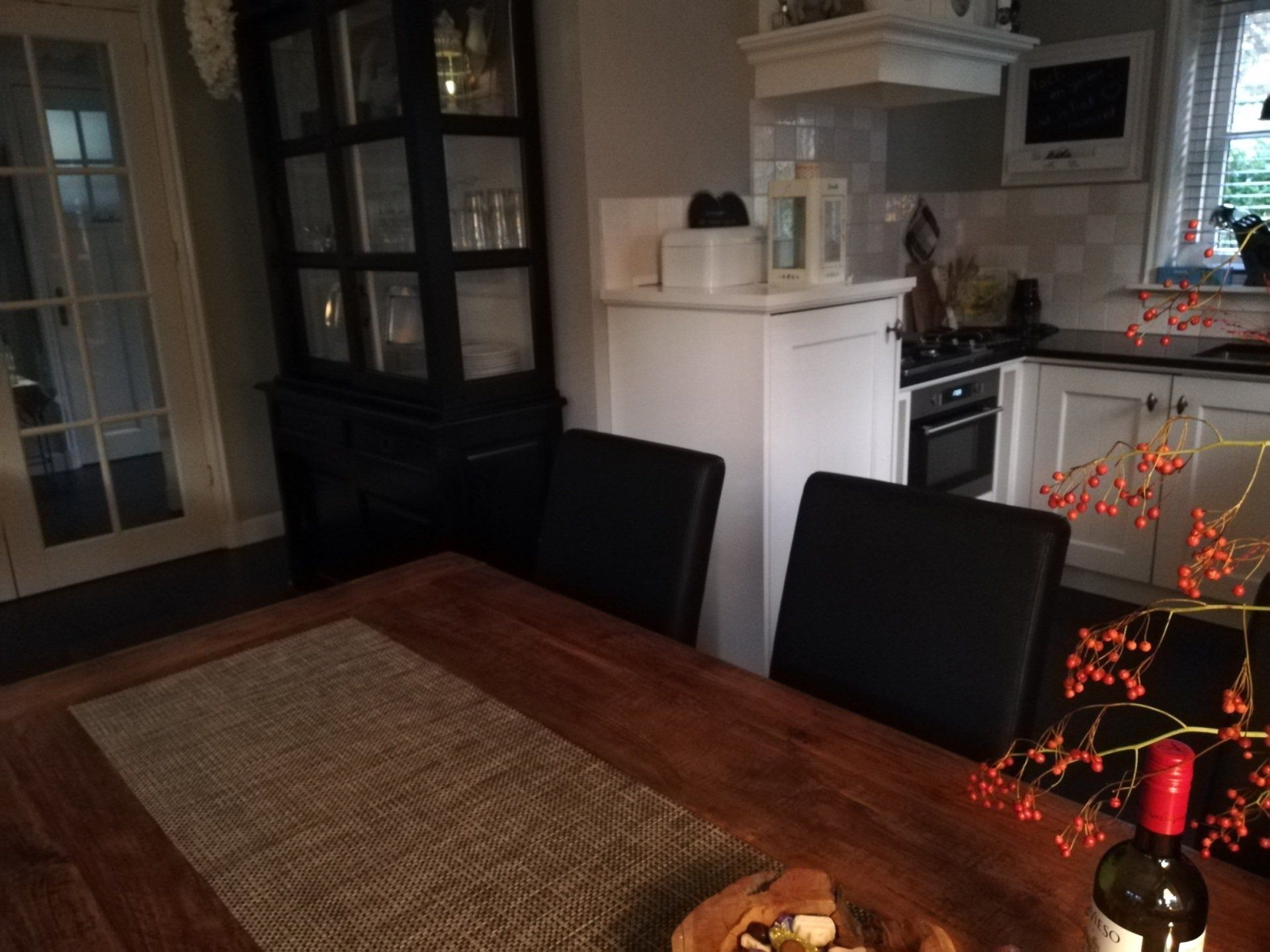 Houten eettafel met twee zwarte stoelen voor een zwart kastje en een witte keuken.