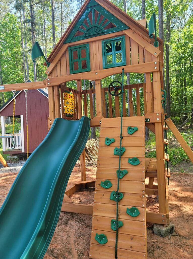A wooden playground with a slide and a climbing wall.