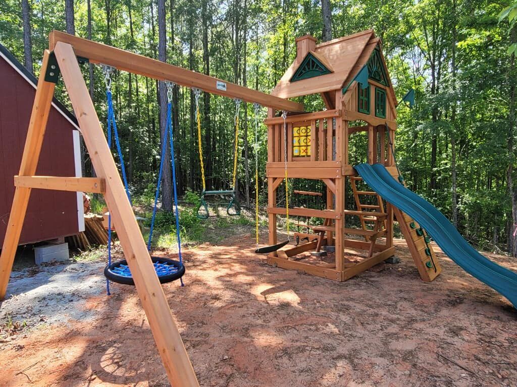 A wooden playground with a slide, swings, and a bird nest swing.