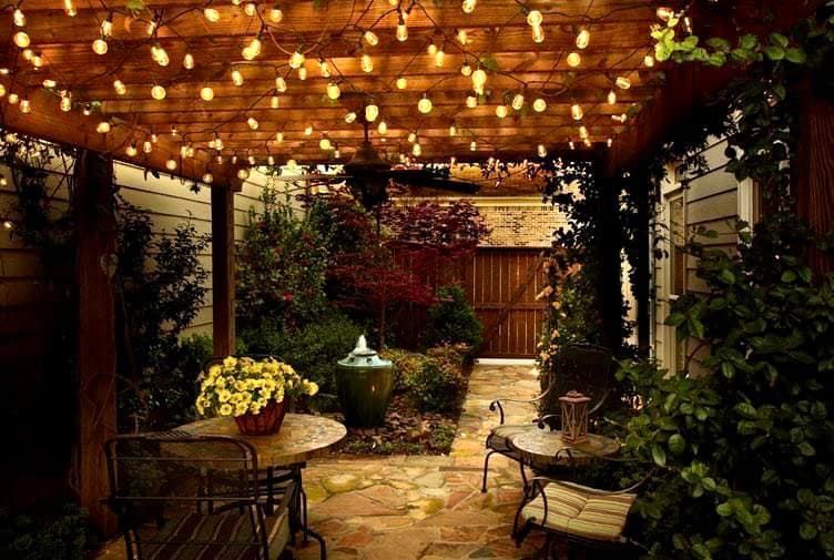 A patio with a table and chairs under a pergola with lights.
