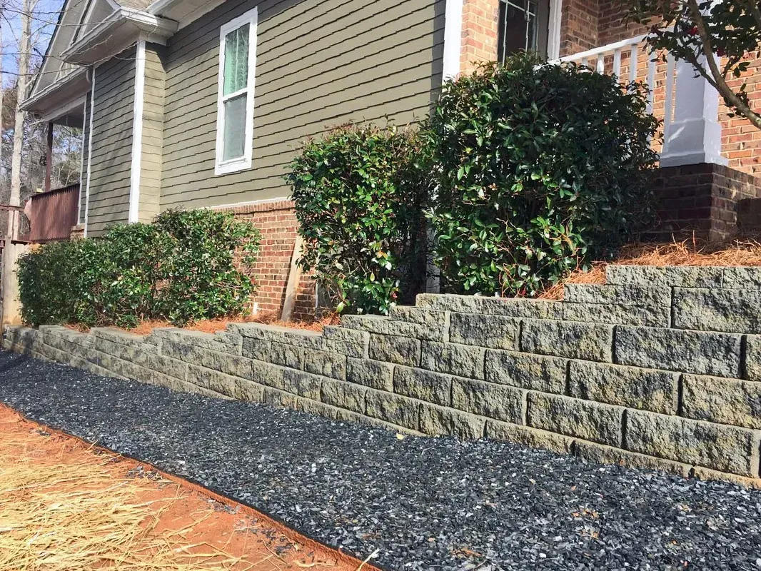 Home exterior with landscaped stone retaining wall, shrubs, and gravel walkway beside siding and brick.
