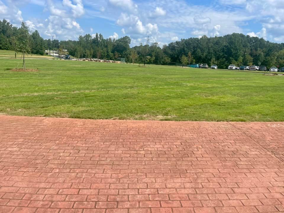 A brick walkway leading to a large grassy field.