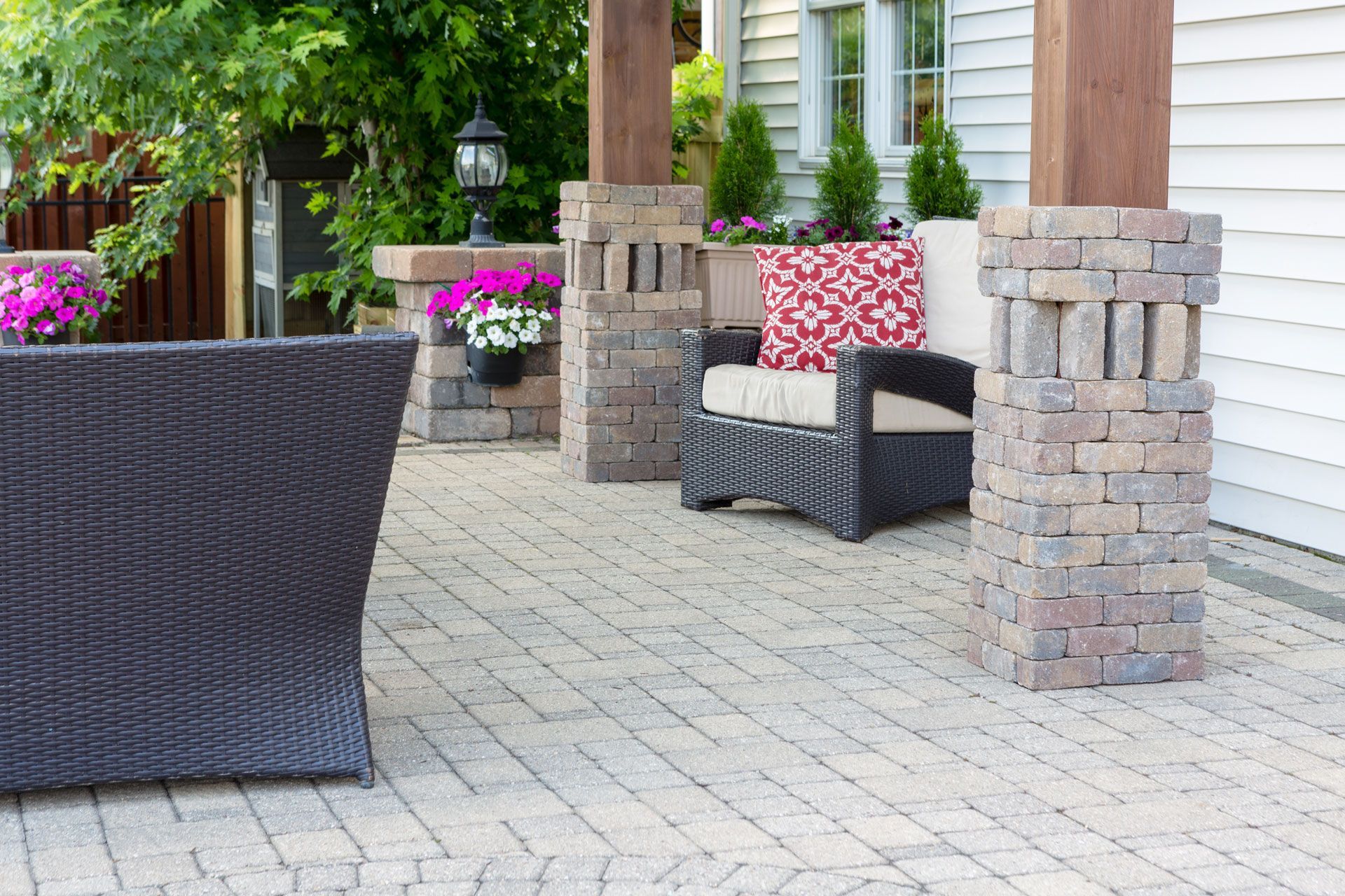 Outdoor patio with wicker chairs, patterned cushions, and potted flowers beside a stone house
