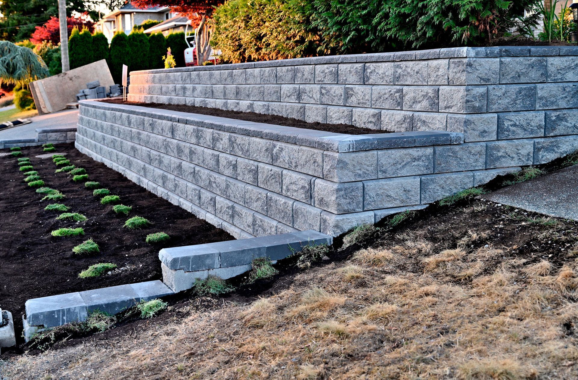 Terraced gray stone retaining wall beside a landscaped garden bed and dry slope
