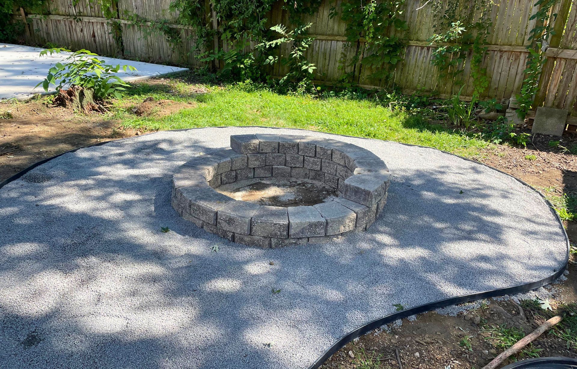 Stone fire pit surrounded by gravel in a sunlit backyard garden