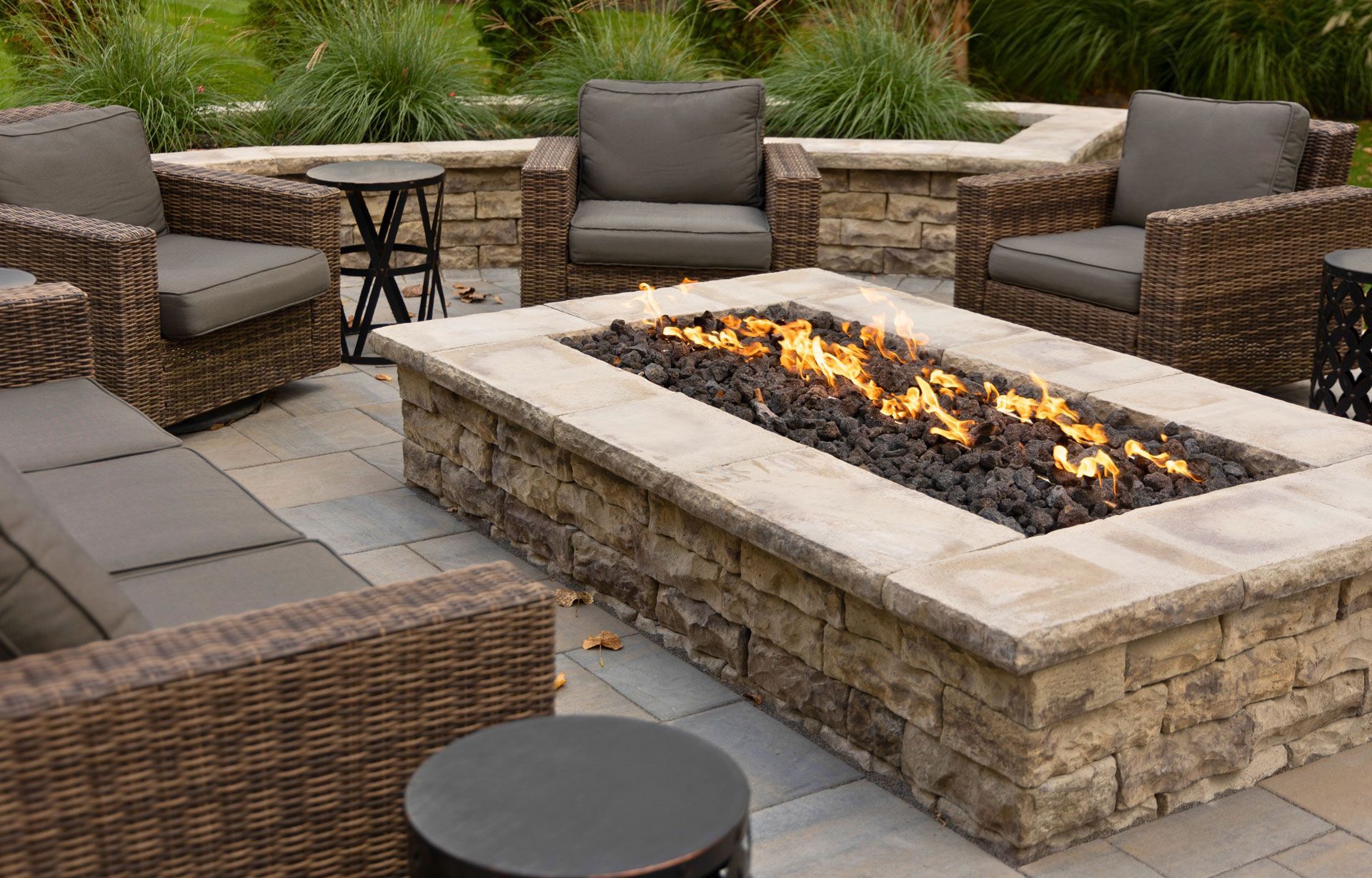 Outdoor patio seating area with wicker chairs around a stone fire pit with flames