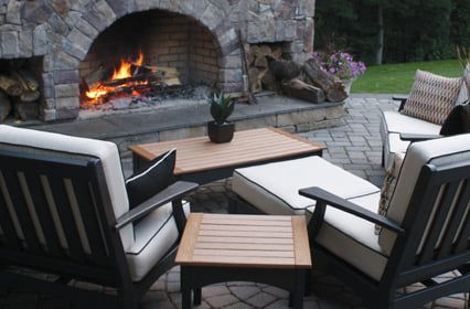 Stone patio with cushioned chairs around a fire pit and small table at dusk