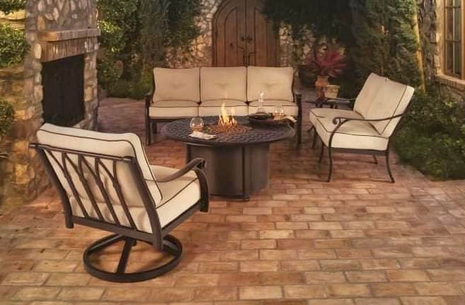 Stone patio with beige outdoor seating around a fire pit beside a brick fireplace