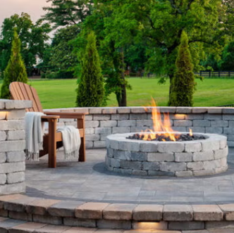 Backyard patio with stone fire pit, wooden chairs, and green lawn in the background