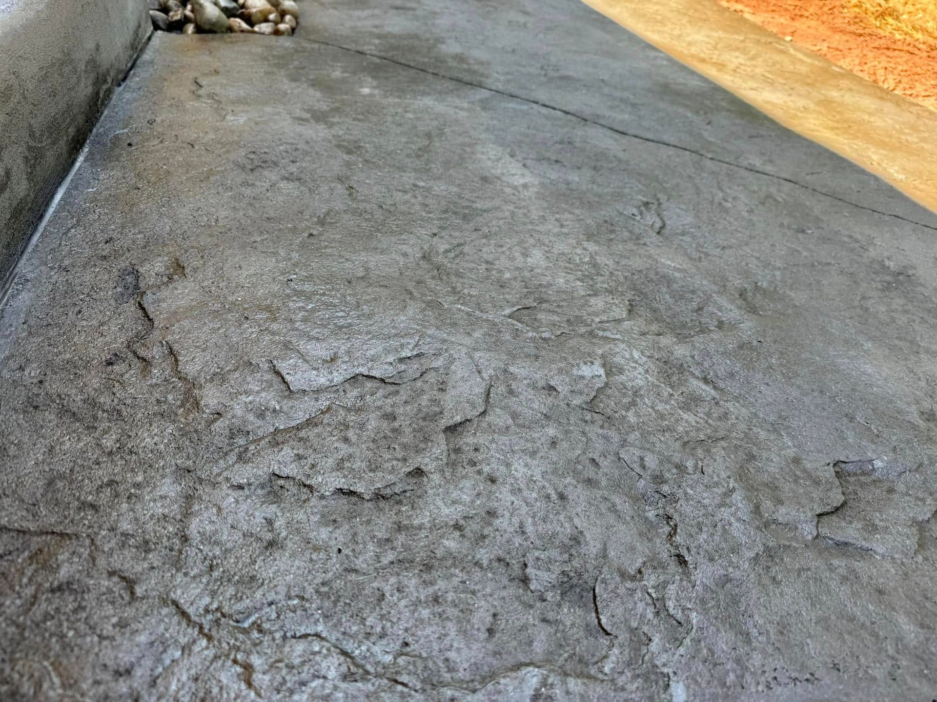 Cracked concrete driveway with a rough, uneven surface and scattered debris near the edge