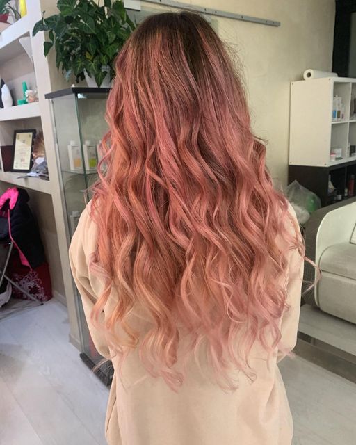Donna con lunghi capelli ondulati color rosa e rosa in un salone.