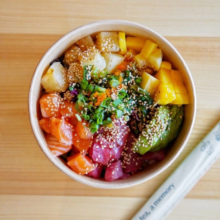 Colorful poke bowl with avocado, mango, salmon, rice, and sesame seeds in a white bowl on a wooden table