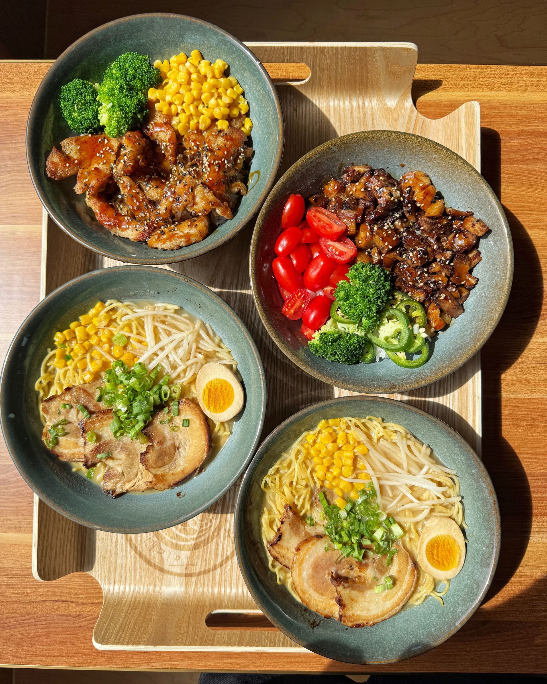 Four bowls of rice dishes on a wooden tray, with broccoli, corn, red peppers, and eggs.