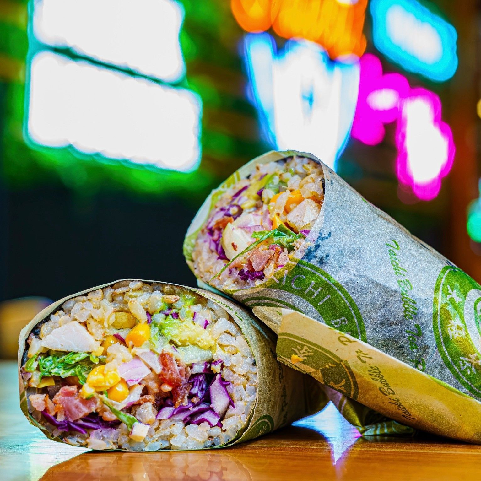 Two veggie burritos on a table with a colorful blurred neon background