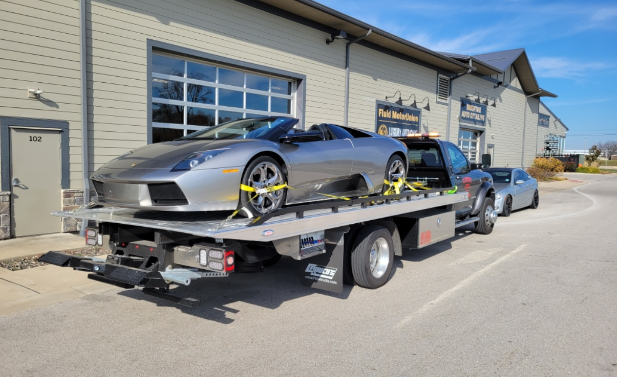 A silver sports car is sitting on top of a tow truck.
