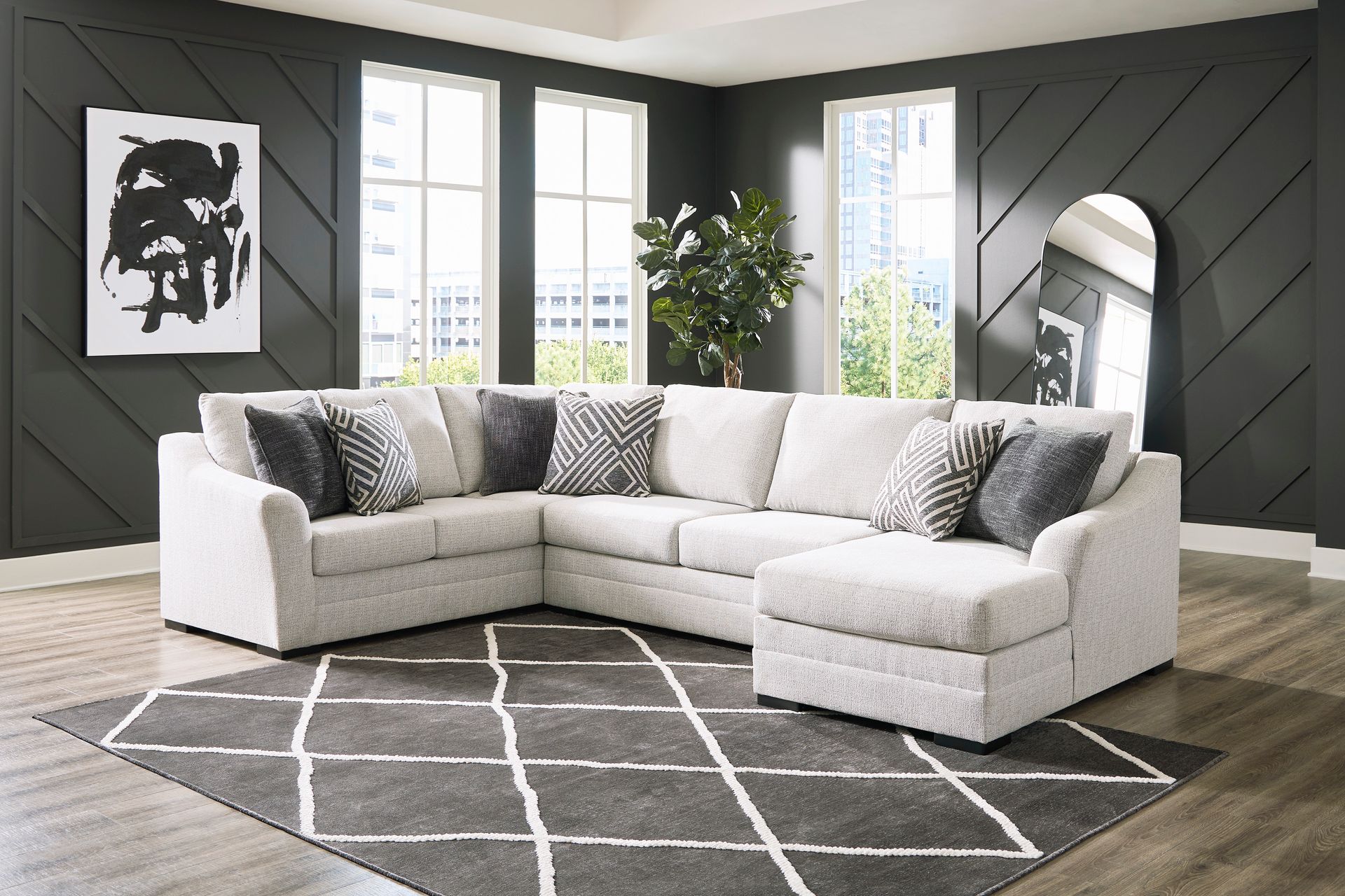 U-shaped cream sectional sofa with pillows on a patterned rug in a room with dark walls and windows.