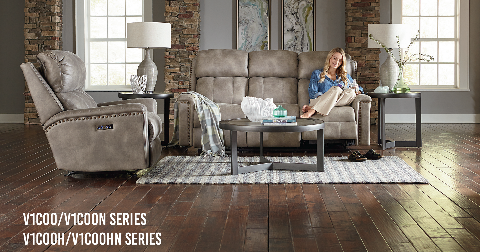 Woman relaxing on a gray sofa in a living room, with a recliner and coffee table.
