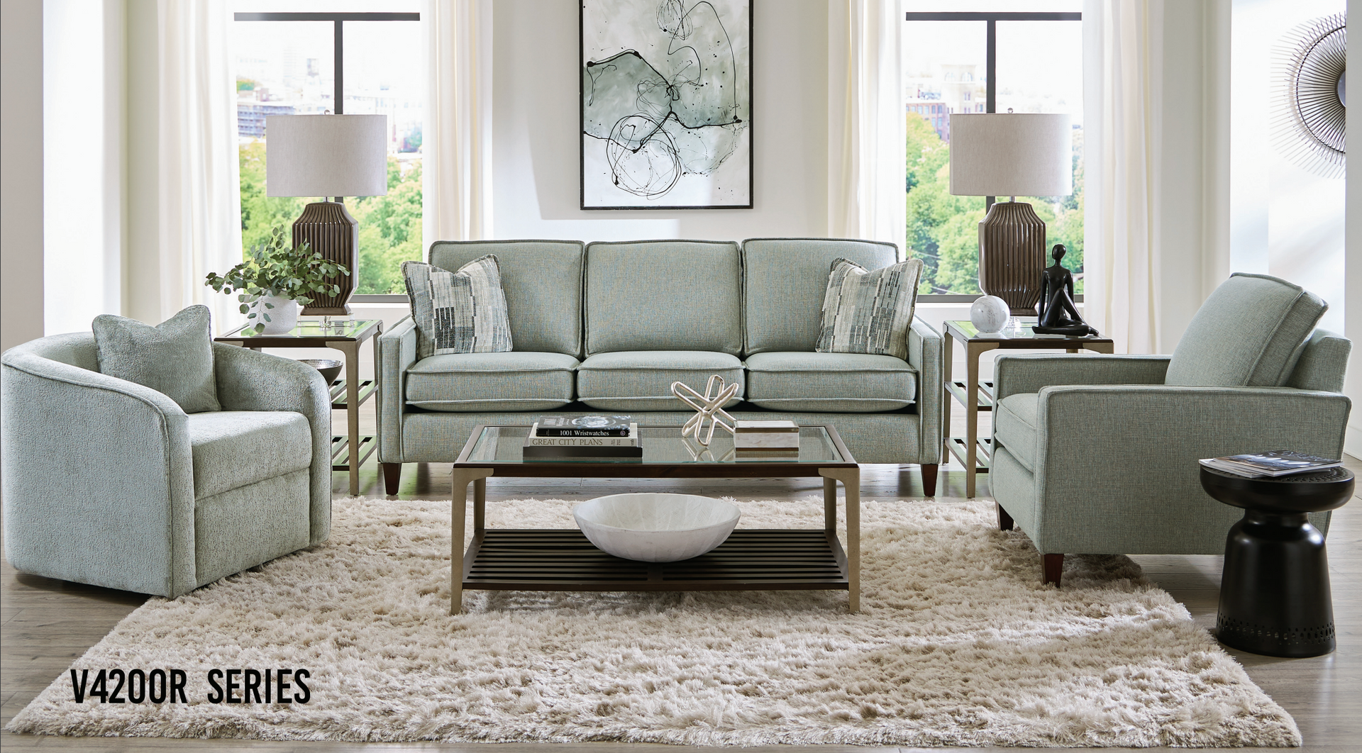 Living room with light teal sofa, chairs, rug, coffee table, lamps, and artwork.