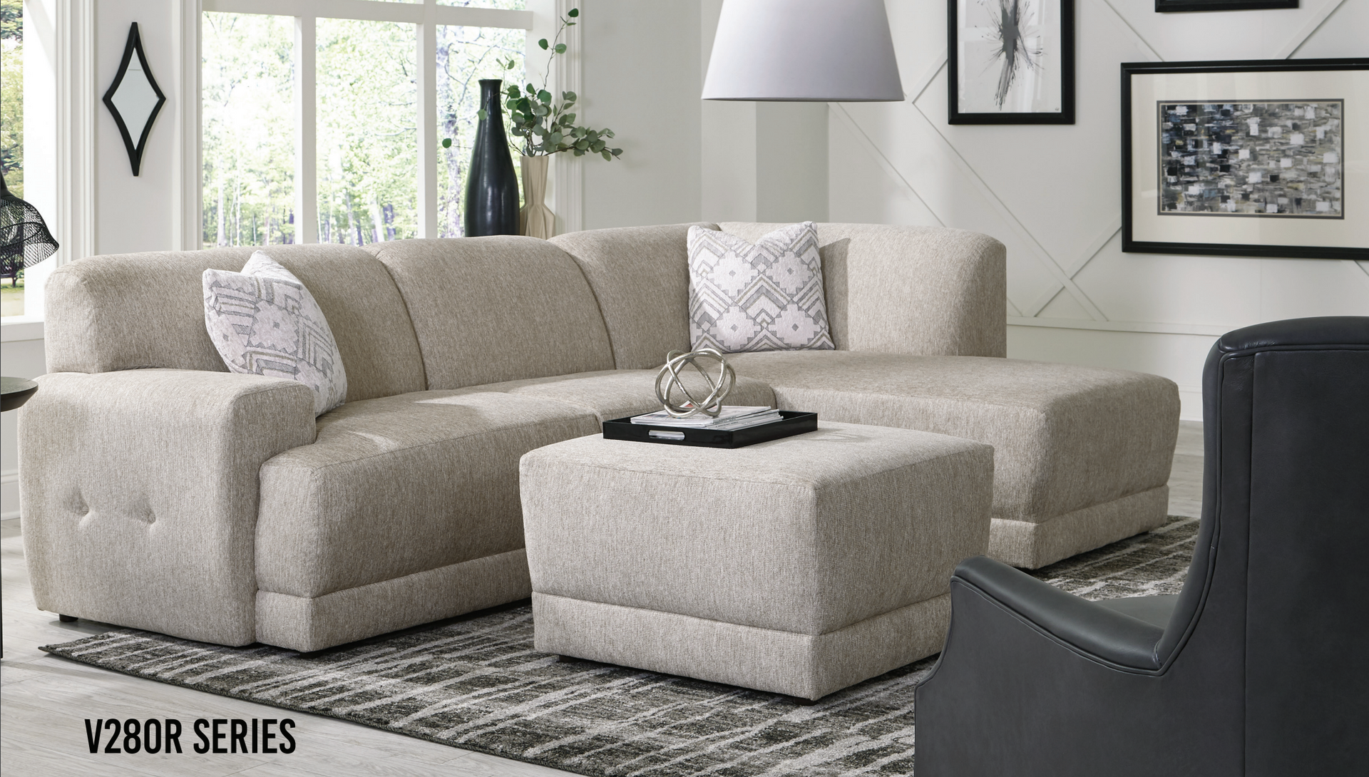 Beige sectional sofa and ottoman in a living room, with decorative pillows and artwork.