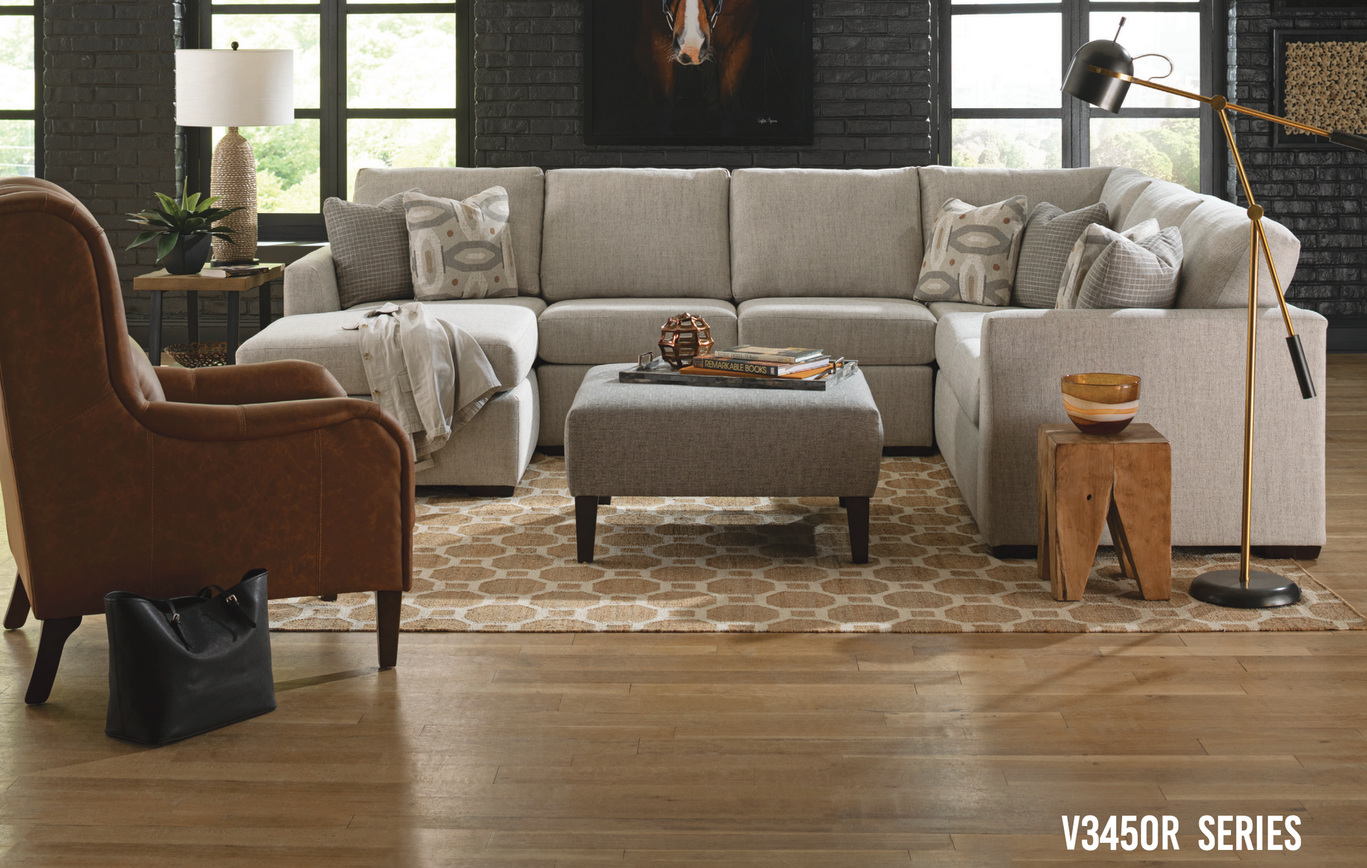 Living room with a light gray sectional, ottoman, leather chair, and wooden side table.