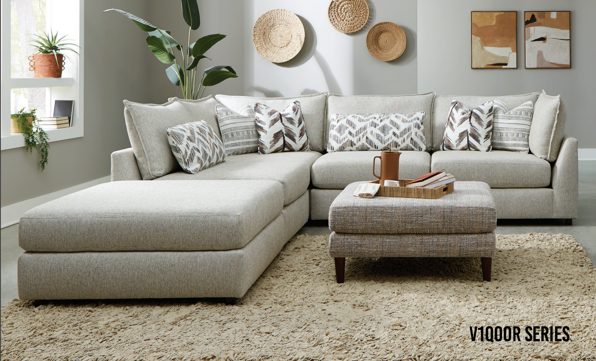 Light gray sectional sofa with ottoman in a living room, decorative pillows, wall art, and a shaggy rug.