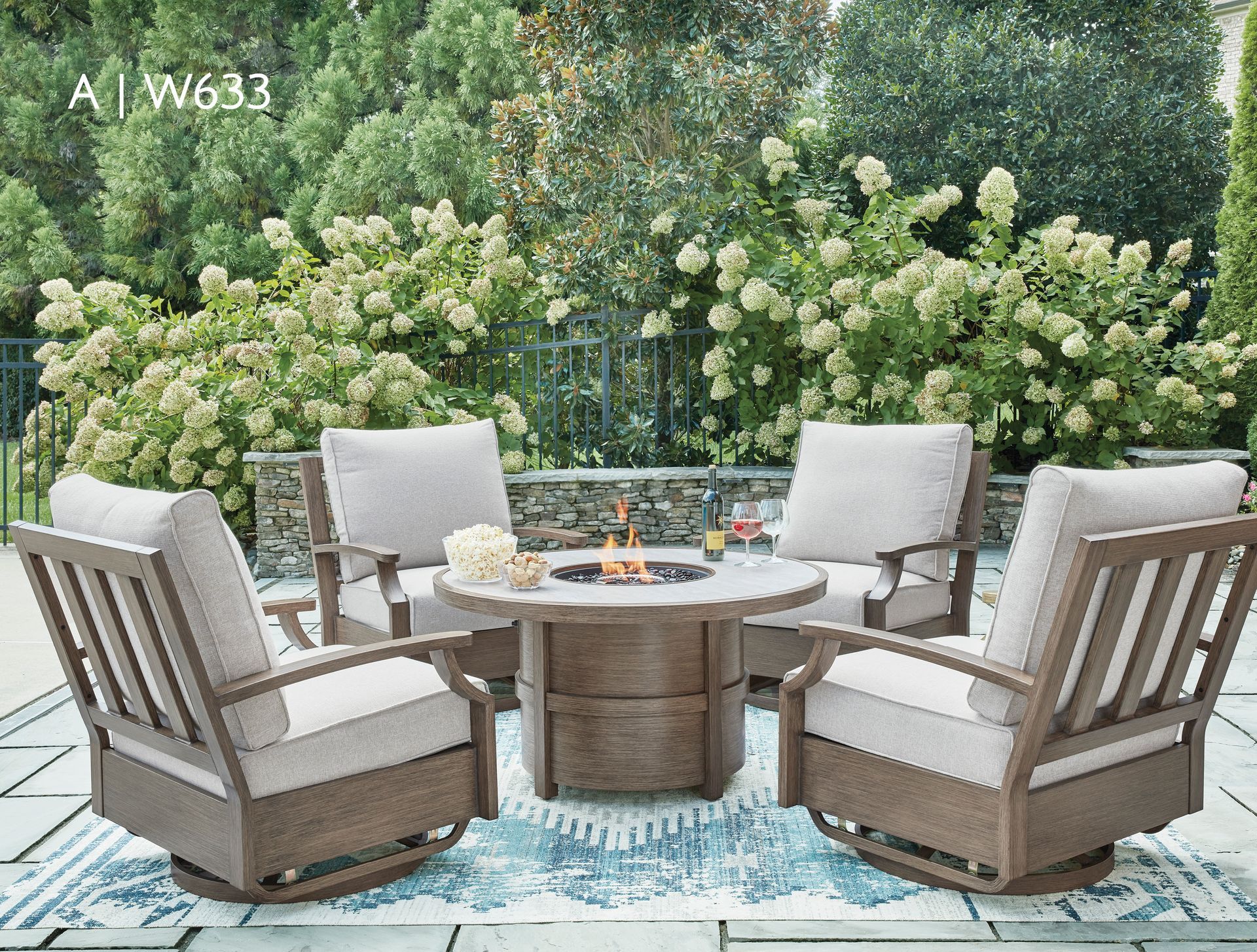 Outdoor patio set with fire pit and four cushioned chairs in a garden setting.