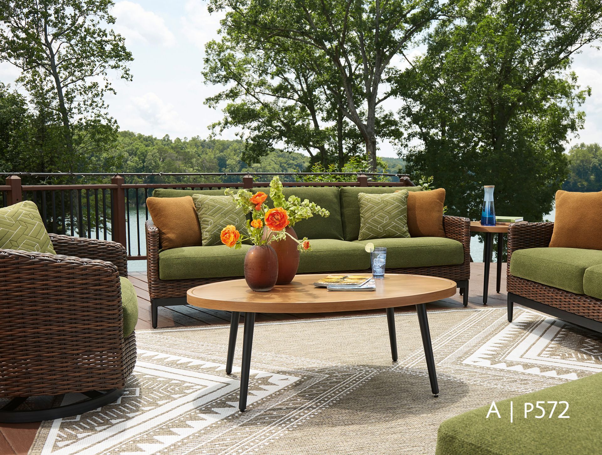 Outdoor patio furniture set on a deck overlooking a lake with green cushions, brown wicker, and a wooden coffee table.