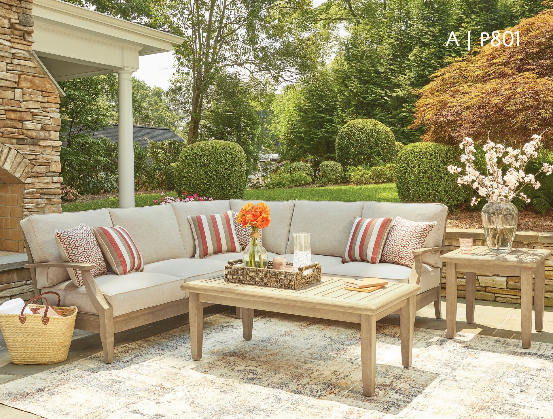 Outdoor sectional seating arrangement with neutral cushions, coffee table, and side table.