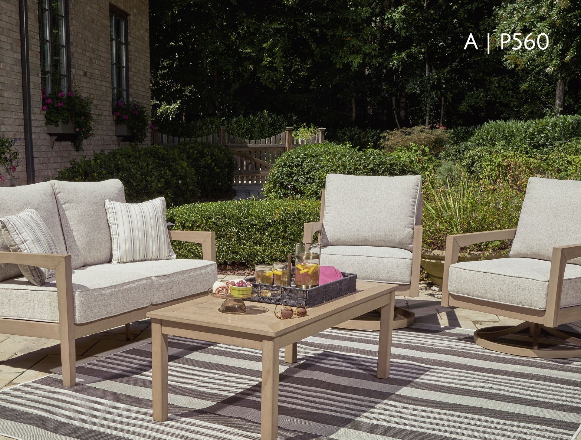 Outdoor seating area with a sofa, two chairs, and a coffee table on a striped rug.