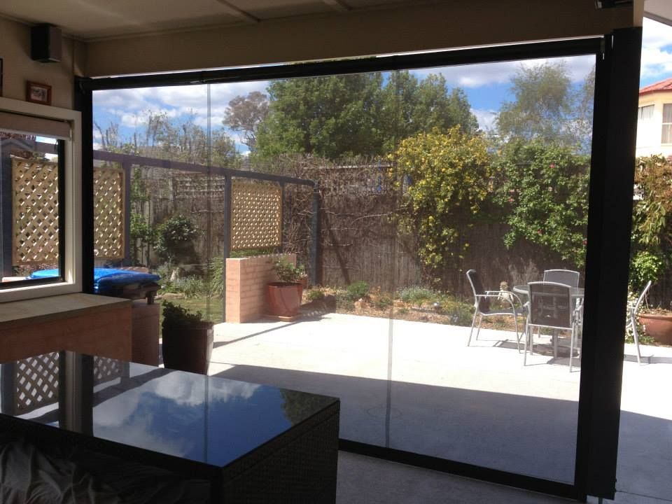 Patio with black framed roll-down sunshade, open, revealing a backyard with a patio set, trees, and fence.