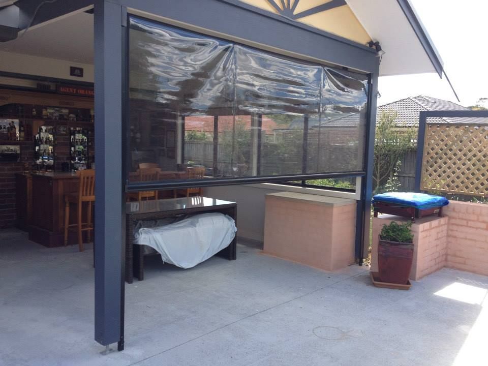 Outdoor patio with roll-down shade, a table covered with a white sheet, and a brick wall.