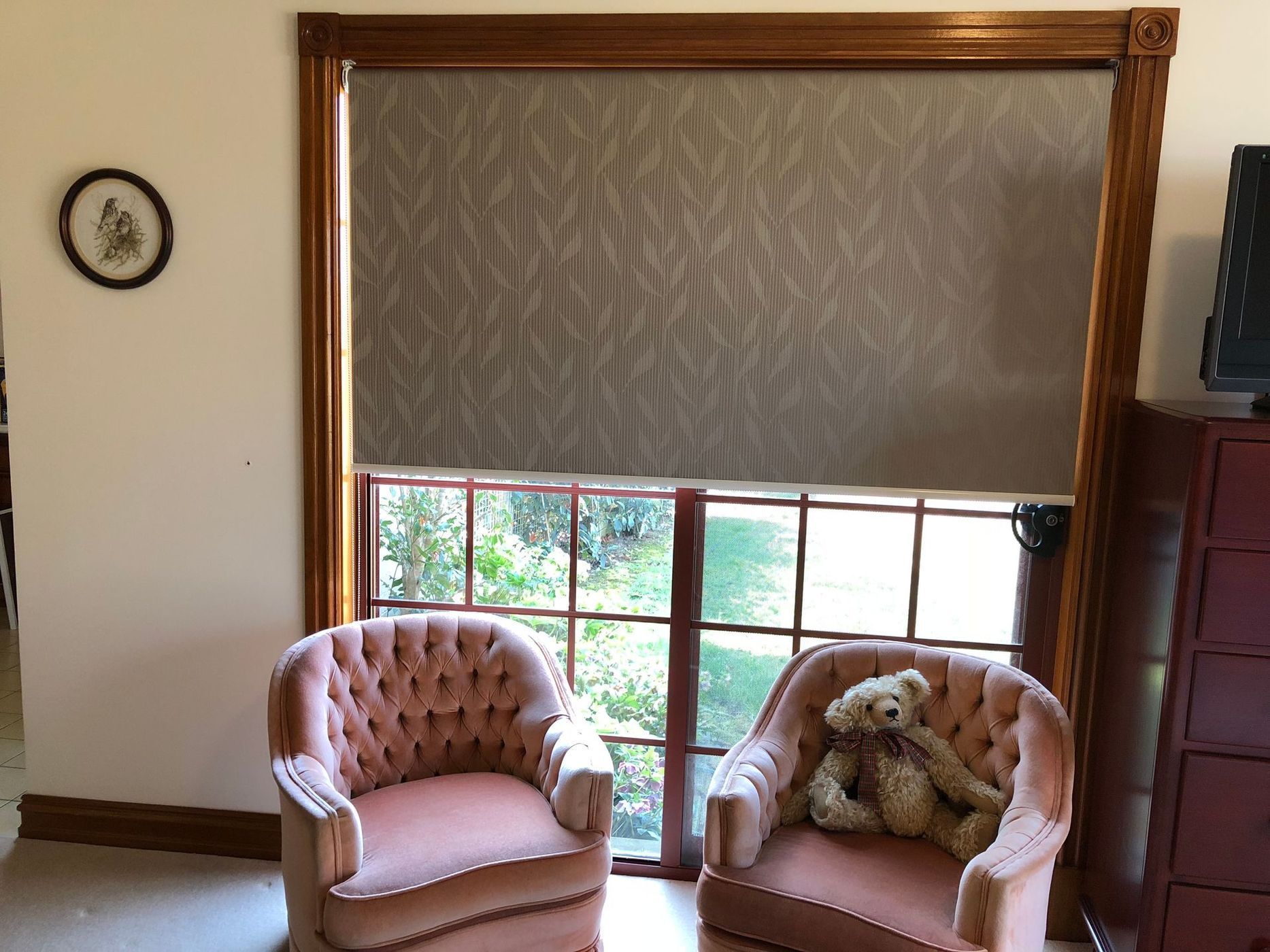 Two pink armchairs face a window with a drawn shade, a teddy bear, and a small framed picture on the wall.
