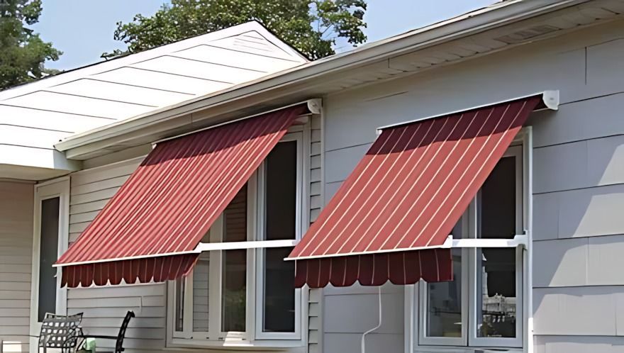 Two windows with red and white striped awnings on a beige house.