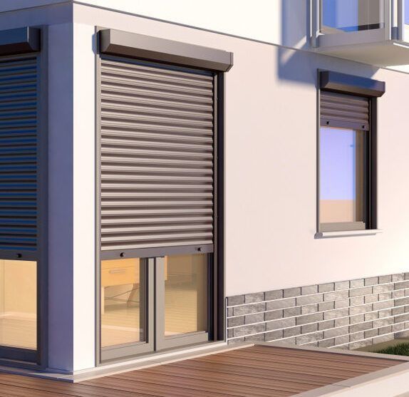 Exterior of a house with two windows featuring brown roller shutters. One shutter is fully closed.