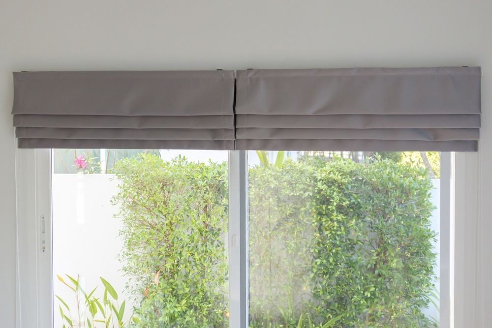 Room with white horizontal blinds, large pendant lamp, and view of green outdoors.