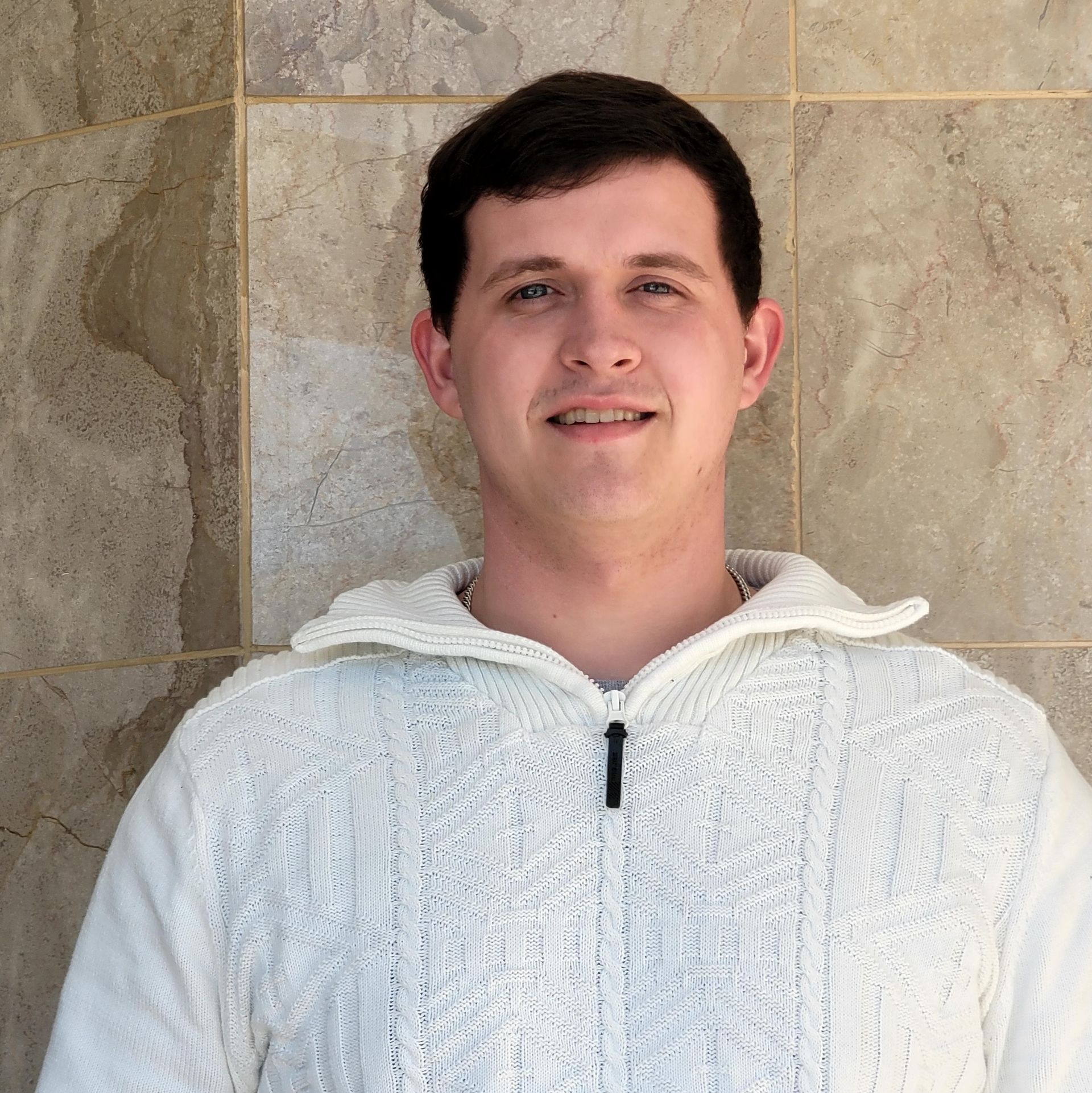 A man wearing a white sweater is smiling for the camera