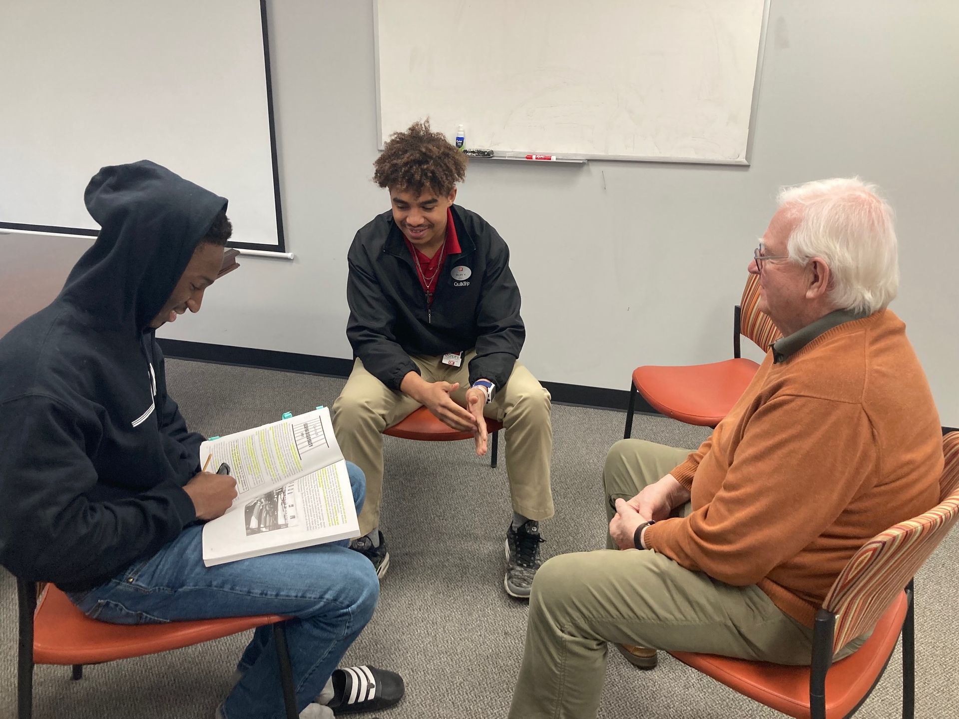 Three people are sitting in chairs in a circle talking to each other.