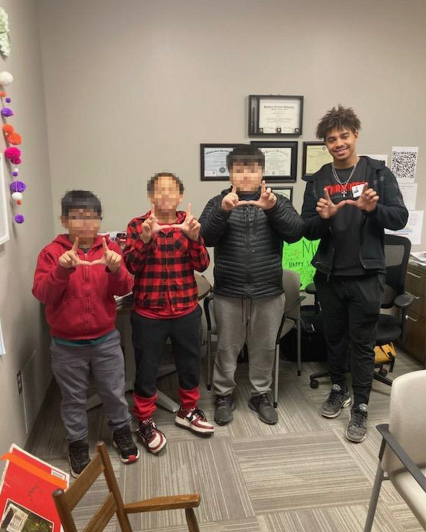 A group of young boys are standing in a room making a heart shape with their hands.