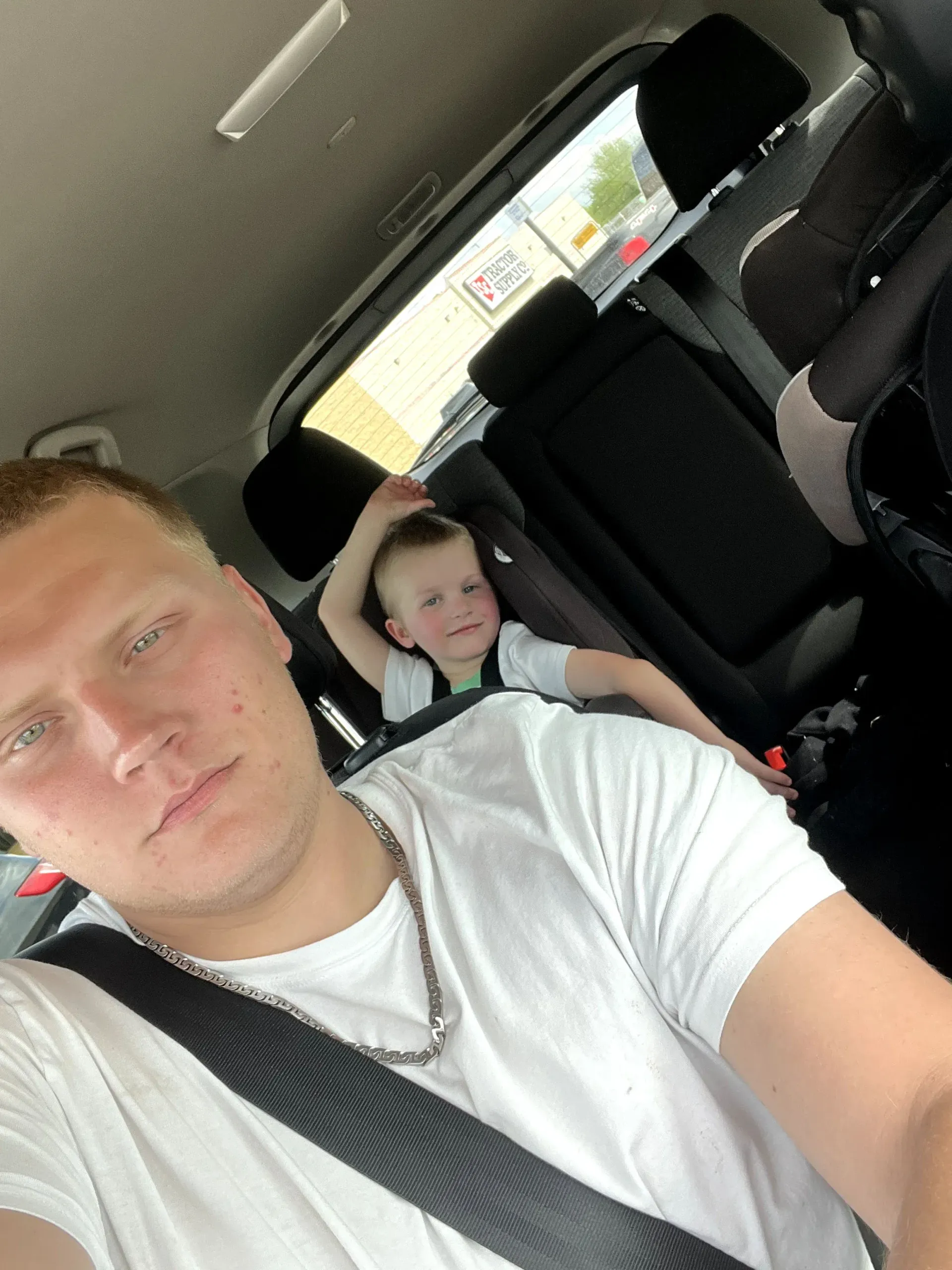 white mail in car with small child smiling from the backseat behind him.