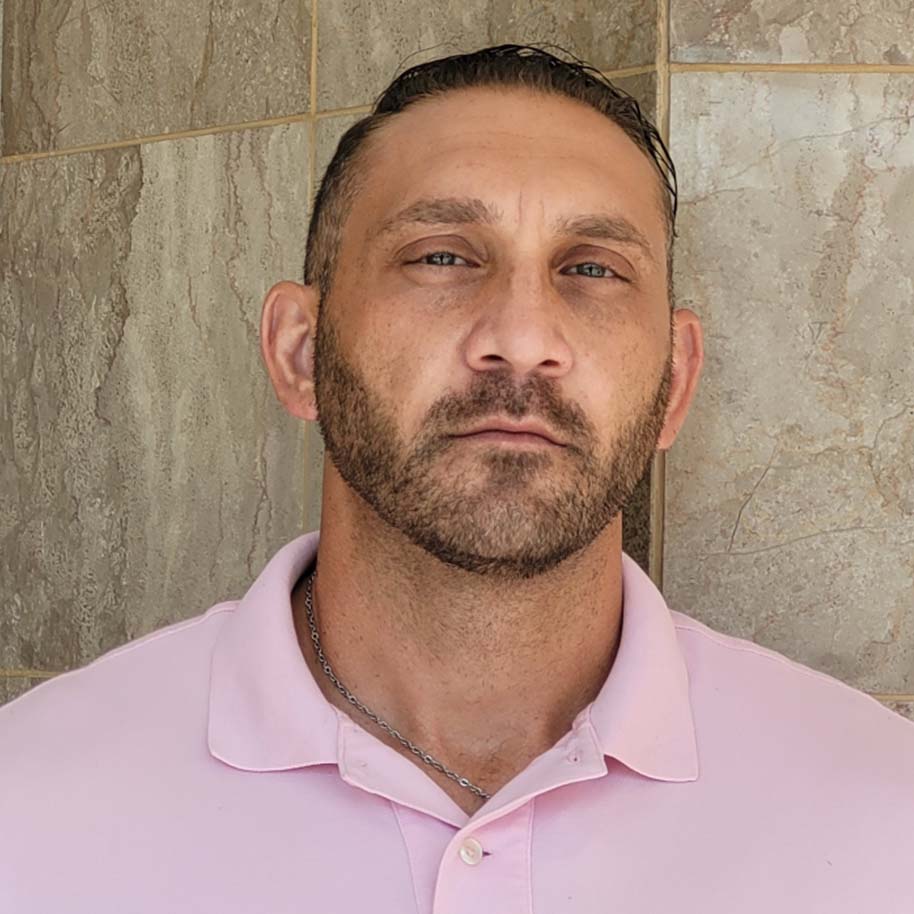 A man with a beard is wearing a pink polo shirt.