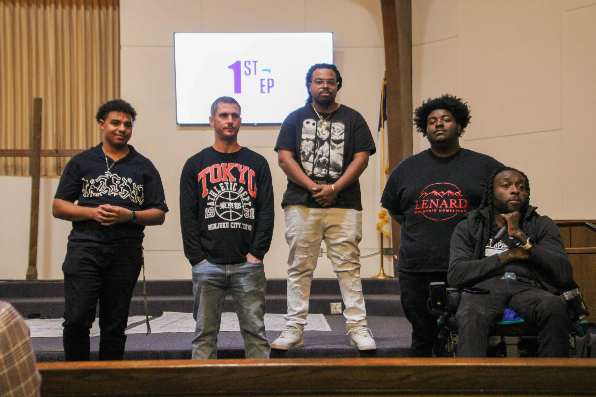 A group of men are standing in front of a screen that says 1st Step.