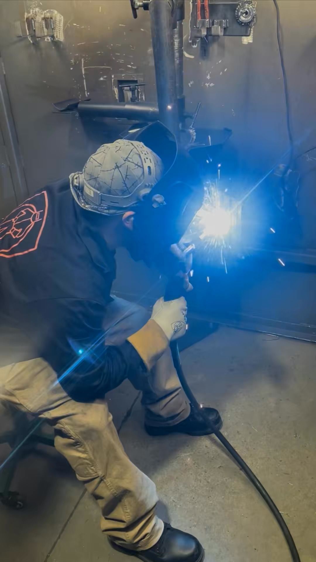 Worker welding metal in a workshop, bright blue sparks illuminating the scene.