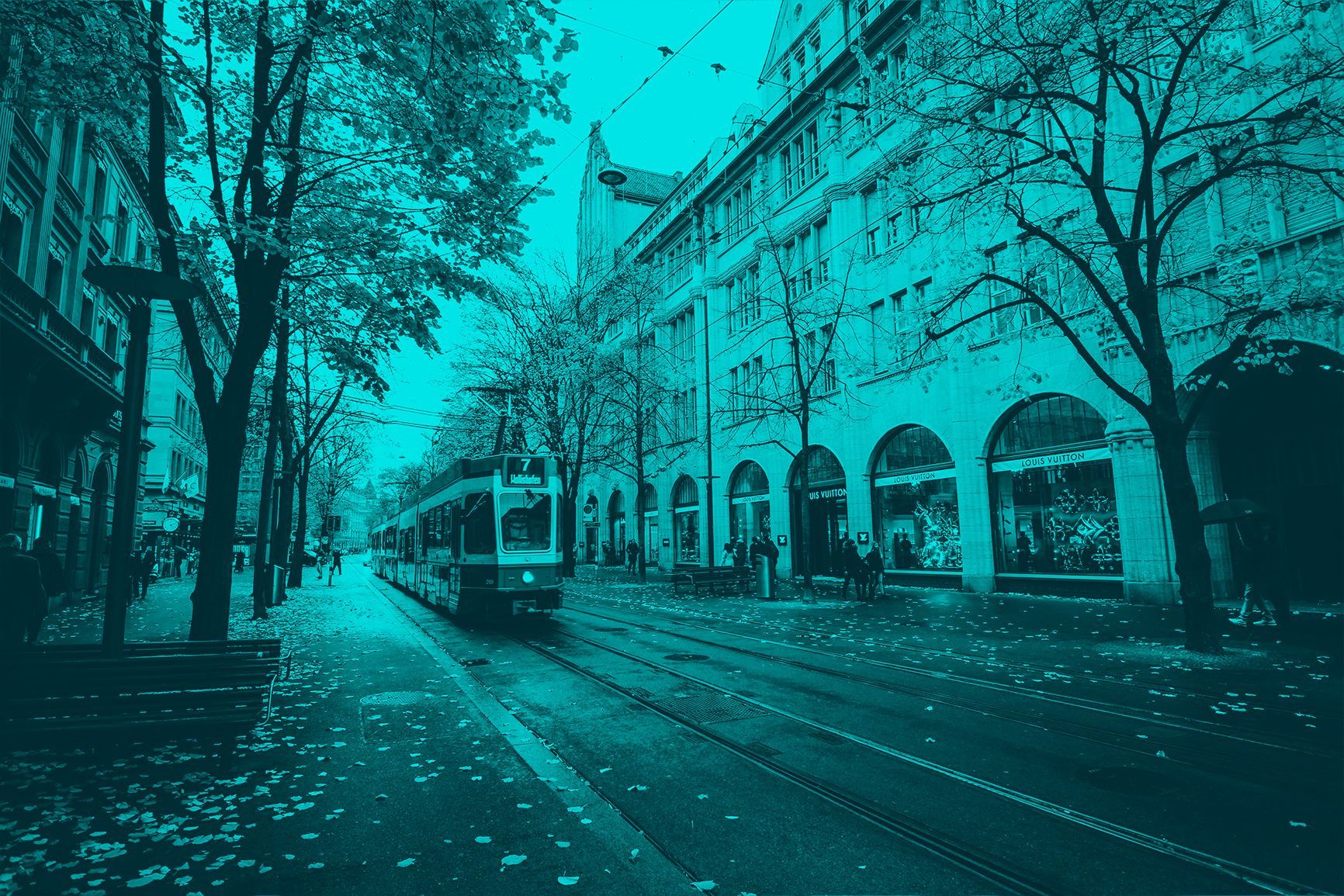 Tram on a tree-lined city street beside arched buildings, tinted blue-green.