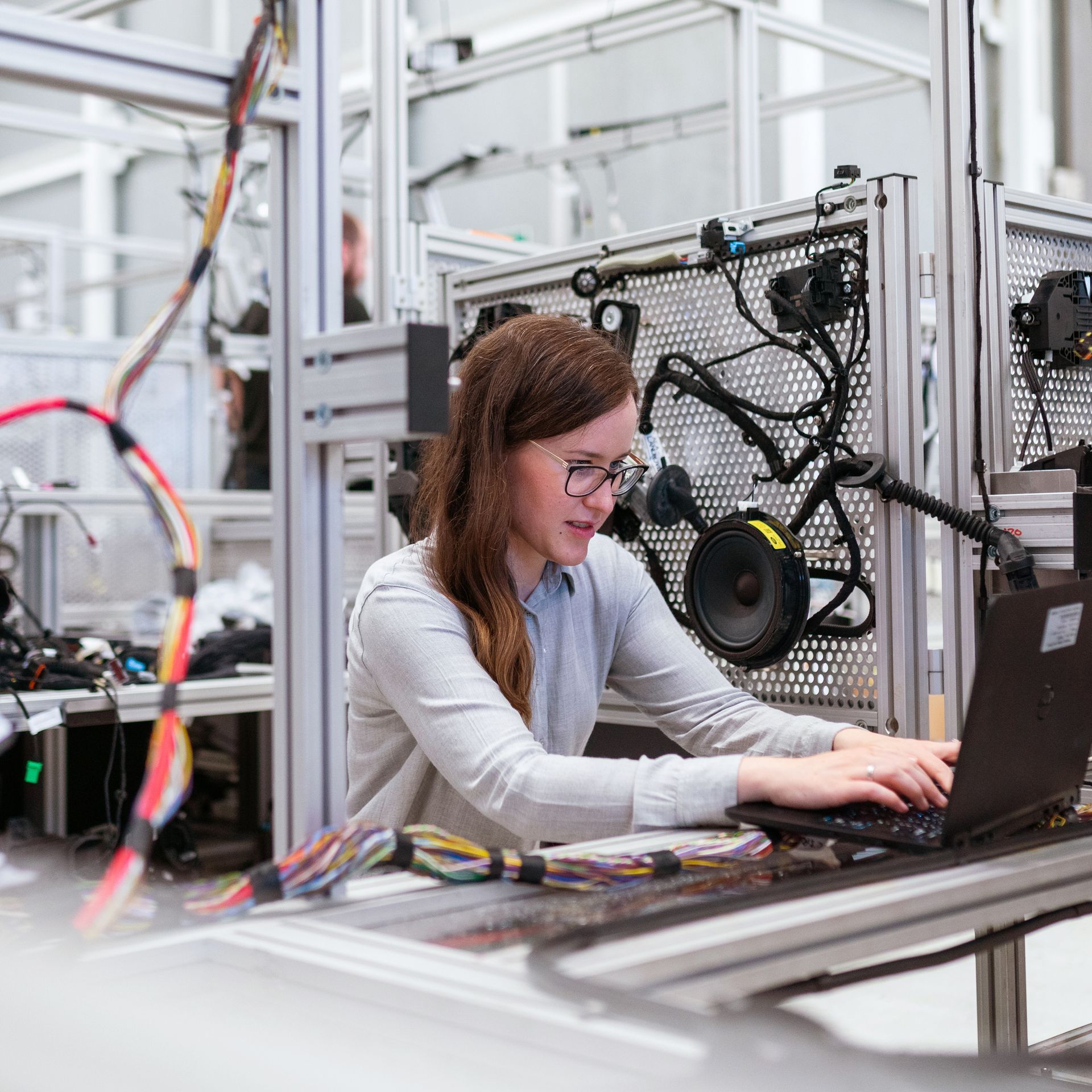 Woman working on a laptop in an industrial lab with machinery and cables nearby